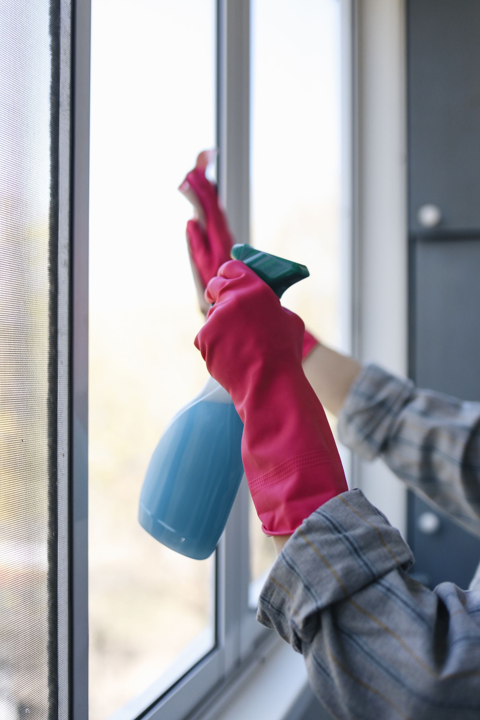 A person cleaning window glass with a cloth and spray bottle